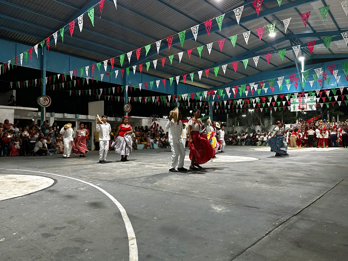 Grupo de baile folklórico con sombreros y faldas de colores, bailando frente a las gradas llenas de público.